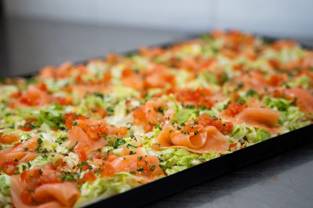 Lachs-Pizza auf dem Blech: frischer rosa Lachs auf zart grünem Eisbergsalat garniert mir gehackter Petersilie