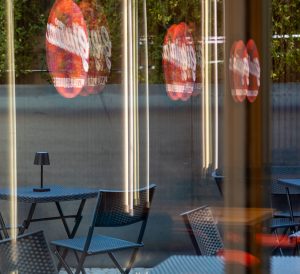 Außenterrasse von Giulia Pizza durch die Scheibe betrachtet, in der sich die Logos vom Innenraum spiegeln