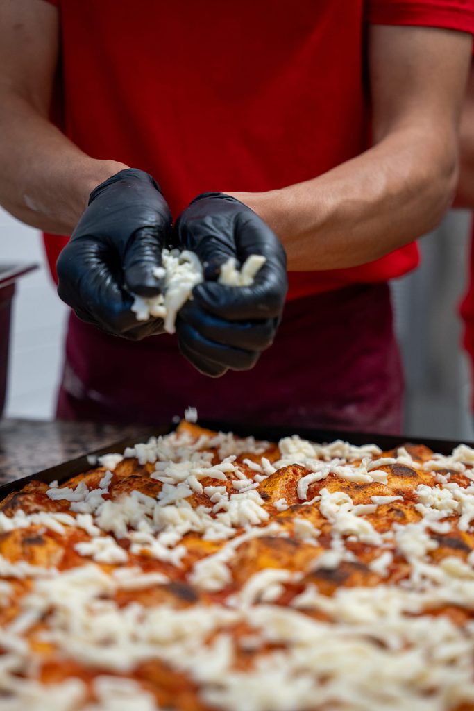 Pizzabäcker beim Bestreuen der Pizza mit Käse